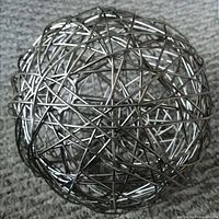 Close-up image of an abstract, spherical sculpture made of tightly woven silver metal wires placed on a carpeted floor.