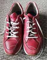 Front view of pair of red leather women's shoes with white laces and stitching on carpeted floor