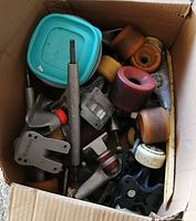 Box of assorted skateboard wheels, trucks, and hardware parts, including a blue container lid inside the box.