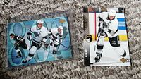 Two hockey cards of Wayne Gretzky laid on a brown carpet, both in protective sleeves. One card has a collage of Gretzky skating and one shows him shooting the puck.
