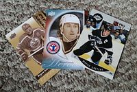 Three Wayne Gretzky hockey cards laid on carpet, showing front faces including Oilers (sepia), white helmet (modern), and Kings (black) uniforms.