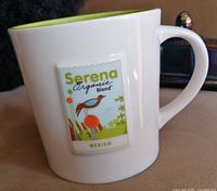 Front side of mug showing a label design with 'Serena Organic Blend' and bird graphic in green and orange colors, white ceramic body with lime green interior.