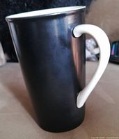 Side view of the tall black matte ceramic Starbucks mug with white handle.