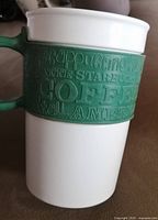 Side view of ceramic Starbucks mug showing green silicone band with embossed coffee-related words.
