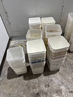 33 white square plastic buckets stacked in columns on a concrete floor, showing their empty interiors and used condition.