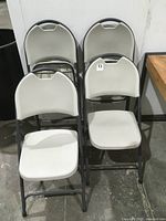 Four gray and black plastic folding chairs stacked together showing front and top view.