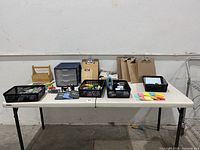 Table display of assorted office supplies including baskets with small items, clipboards, Post-it notes, calculators, scissors, and a Sterilite organizer.