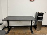Black rectangular desk against white wall with two round cord grommets on tabletop corners, metal legs, and stable base.