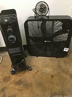 Photo showing the black Utilitech 21-inch box fan, small black USB-powered Malmko desk fan placed on top, and the black Intertek radiating heater positioned next to them.