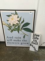 Framed poster and small wooden sign shown together. Poster depicts white flower with quote, wooden sign reads 'live life in full bloom'.