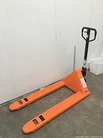 Full view of orange pallet jack leaning against white wall