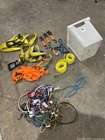 Full lot on floor showing yellow Husky ratcheting straps, orange tie down straps, assorted bungee cords, and white container