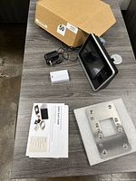 Overview of the time clock unit, power adapter, mounting plate, manuals, and box on table