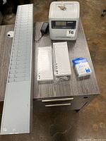 Overview photo showing Pyramid 4000 time clock, gray metal wall-mounted rack for time cards, packs of time cards, ribbon box, and keys on a table.
