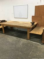 Full view of the wooden workbench showing the main tabletop and attached side shelf with two metal vices on the workbench ends.