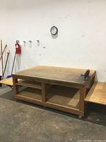 Front view of the wooden workbench showing flat main tabletop, foldable side shelves extended, and storage shelves below.