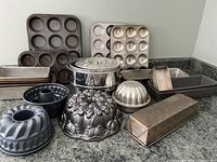 Full assortment of baking pans and molds displayed on countertop showing muffin tins, loaf pans, Bundt pans, springform pan, and decorative cake molds.
