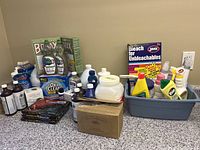 Overview of assorted cleaning and laundry supplies on counter and in plastic bin showing various brands and product types