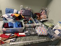 Overview of large lot including bins of fabric pieces, plastic bags with folded fabric, and some completed quilt blocks on a countertop.