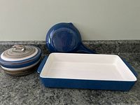 Blue cast iron lasagna dish, skillet, and ceramic casserole dish with lid on granite countertop