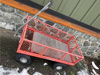 Full view of the red metal garden wagon with mesh sides and base, black handle, and four tires.