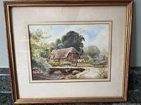Full image of framed watercolor painting showing rural scene with cottage, bridge, and trees.