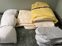 Photo showing rolled and folded quilt batting material in off-white and beige tones along with pre-cut shapes for oven mitts including silver reflective lining.