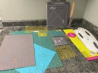 Full view of the lot items on a counter: quilting mats in various colors and sizes, quilting rulers, templates, and wooden-handled sewing tools in a stand.