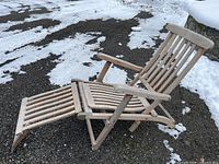 Weathered teak steamer style lounge chair on gravel with snow in background, showing entire chair extended with leg rest.
