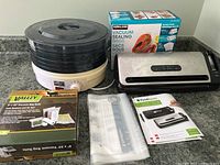 Full view of Salton dehydrator with multiple black trays and FoodSaver vacuum sealer machine with vacuum bag boxes and manual on countertop.