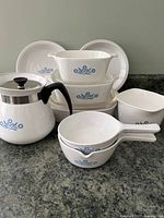 Full lot photo showing all Corningware pieces arranged on countertop including coffee pot, covered casseroles, mixing bowls, serving bowls, and plates.