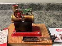 Front view of Mamod Minor 1 steam engine with wooden base, showing boiler, flywheel, chimney and fuel tray