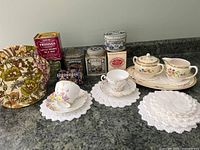 Overview of the vintage tea party items showing tea tins, teacups, sugar bowl, creamer, doilies, and tea cozy.