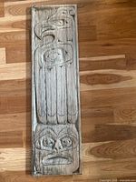 Full view of the carved cedar plank showing bird on top and face on bottom