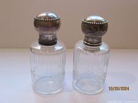 Pair of antique glass dresser bottles with detailed sterling silver lion stoppers shown from the front, clear glass with patterns on the lower half, sizing approximately 5 inches tall.