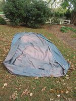 Full view of the grey car cover laid out on grass and leaves, showing overall size and condition.