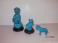 View of the three porcelain figurines together showing the Foo Dog, cat, and horse with turquoise blue glaze and wooden stands for the first two items.