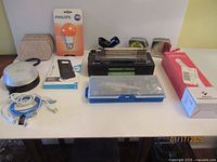 Photo showing various items including Philips LED bulb, Medic Therapeutics sterilizer wand, phone case, emergency rescue kit, screwdrivers, folding rulers, tape measure and cables on a table.