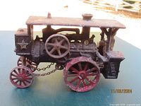 Side view showing rusted cast iron structure, red spoked wheels, hull details, chains connecting wheels and star emblem on side.