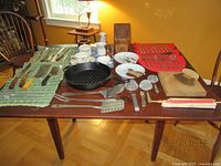 Full table view showing broad assortment of vintage and cast iron kitchenware items including cutlery, pans, bowls, and utensils