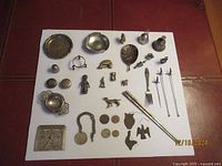 Full view of all mixed metal items laid out including coins, small figurines, chopsticks, fork, cocktail stirrers, and brass lock.