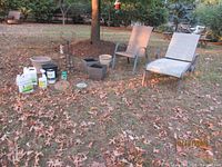 Image showing aluminum sling chase lounge chair with visible wear, multiple flower pots, gardening supplies including Liquid Fence containers, two shepherds hooks and a wrought iron garden hose holder displayed on a lawn with fallen leaves.