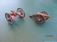 Two toy artillery cannons placed on a flat surface showing front and side views, highlighting wheels and barrel design.