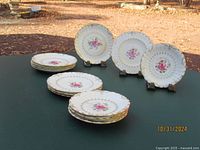 Four stacks of plates outdoors on a green table with several plates displayed upright showing floral pattern with gold trim.