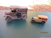 Two vintage cast iron Coca Cola delivery trucks on outdoor table, showing rust and wear