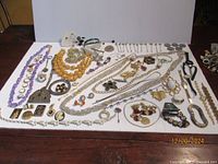 Wide view of over 50 pieces of mixed costume jewelry including necklaces, bracelets, rings, pins, brooches, and watches displayed on a white board.