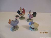 Group of four whimsical ceramic rooster figurines with barnyard characters on springs, all on a flat surface.