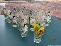 21 individual Looney Tunes glasses arranged on outdoor table showing various characters and designs from the Pepsi Collector Series in new condition.