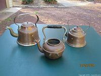 Three antique copper teapots displayed on outdoor table, showing varied sizes and condition.