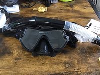 Photo showing the black snorkeling mask with tempered glass lenses and black snorkel with clear flexible tube on a wooden surface.